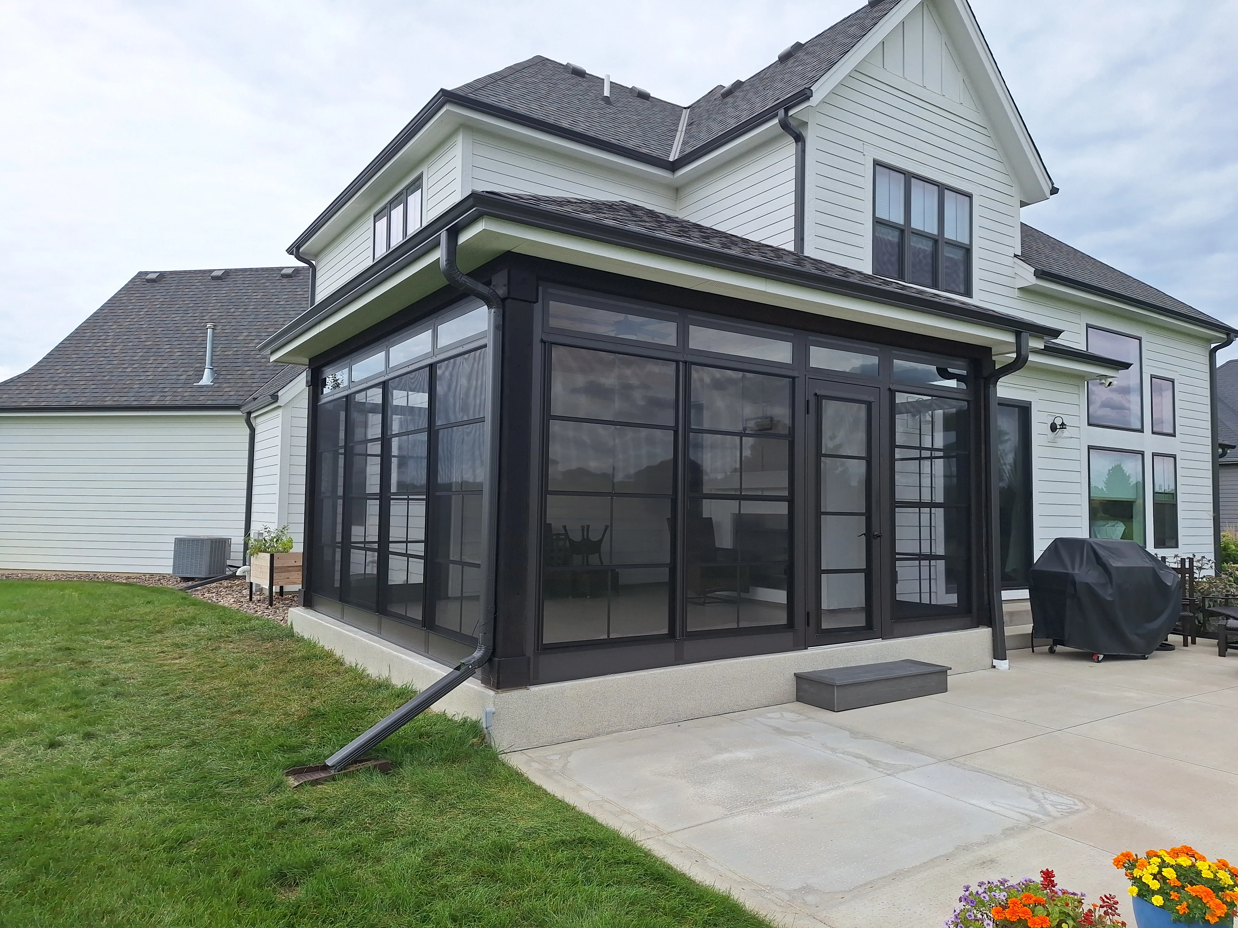 Screened porch addition with black framing beside a white home